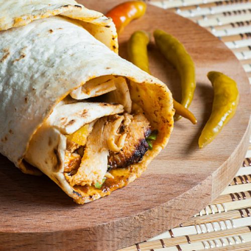 Chicken wrap doner kebap in lavash pita bread durum with thin green pepper pickle on wooden platter. Turkish shawarma, traditional food